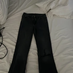 Svarta jeans från ONLY med slitning - Svarta jeans från ONLY i storlek S/34 med cool slitning på ena benet. Klassisk femficksmodell och knappstängning. Jeansen har en rak passform och är gjorda i mjukt denimtyg som sitter skönt hela dagen.