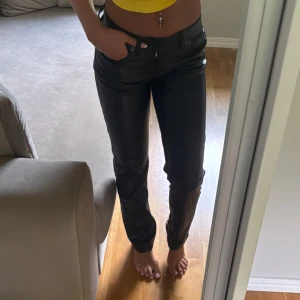 Svarta raka byxor i skinnimitation - Snygga svarta byxor i skinnimitation med raka ben och klassisk femficksdesign. De har midwaist och sitter riktigt bra på. Stora i storleken! 