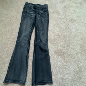 Bootcut jeans i mörkgrå från H&M - Snygga bootcut jeans från H&M i en mörkgrå tvätt med coola slitningar framtill. Modellen har klassiska fem fickor och en elastisk midja utan knapp eller dragkedja. Perfekt för dig som gillar retrovibbar och vill ha en bekväm passform.