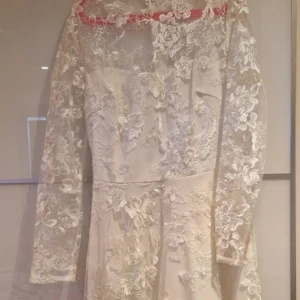 Vit långklänning med spets och blommor - Superfin vit långklänning med transparenta långärmar och detaljerad spets med blommigt mönster över hela klänningen. Klänningen har en romantisk vibe med vacker broderad spets och en mjuk, flowy kjol. Perfekt för speciella tillfällen!