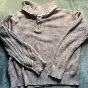 Beige stickad half zip-tröja från Grunt - Säljer en beige stickad tröja från Grunt i storlek L. Tröjan har en snygg krage och half zip-dragkedja framtill. Den är ribbstickad vid ärmslut och nederkant, med långärmade ärmar och en loose passform. Perfekt för chill höst- och vinterdagar.