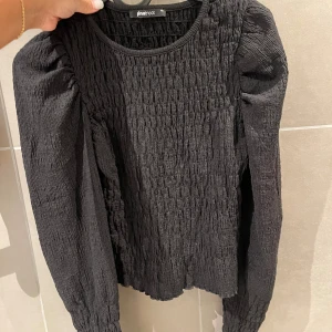 Svart blus med puffärm från Gina Tricot - Säljer en svart blus från Gina Tricot i storlek XS. Blusen har lång puffärm och är helt smockad med en cool textur. Rund halsringning och stretchigt material som sitter snyggt. Perfekt för dig som gillar trendiga detaljer och vill sticka ut.