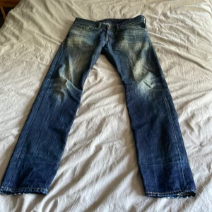 Blå jeans från Diesel Industry - Säljer ett par snygga blå jeans från Diesel Industry med slitna detaljer och coola tvättade effekter. Klassisk femficksmodell med raka ben och kontrastsömmar. Passar dig som gillar en avslappnad och trendig stil. Storlek W29 L32.