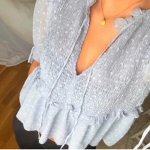 Ljusblå  blus med volang - Superfin ljusblå blus med volangdetaljer. Blusen har v-ringning med knytband och transparenta ärmar i trekvarts längd. Perfekt för dig som gillar romantisk och söt stil!