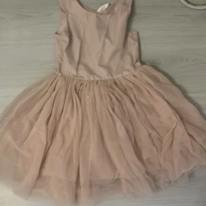 Ljusrosa glittrig klänning från H&M - Supersöt ljusrosa klänning från H&M med glittriga detaljer. Klänningen är ärmlös och har ett fluffigt, voluminöst kjolparti i tyll som ger en riktigt drömmig look. Perfekt för dig som vill sticka ut med en feminin och lekfull stil.