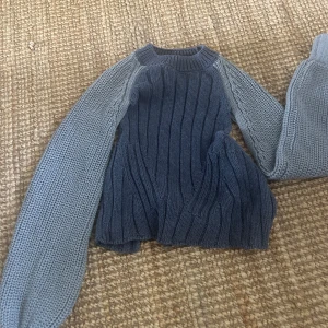 Mörkblå stickad tröja med knyte i ryggen - Säljer en ribbstickad kofta i mörkblått med ljusblå ärmar. Koftan har långa ärmar och ett snyggt knytband där bak. Tröjan har helöppen rygg och är aldrig använd 