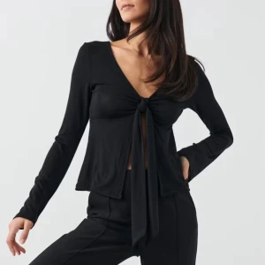 Svart långärmad knytblus från Gina - Trendig svart långärmad blus från Gina med djup v-ringning och snygg knytning framtill. Modellen är croppad och har en mjuk, följsam passform som ger en cool och avslappnad vibe. Perfekt att styla med höga byxor eller kjol. Skriv privat för fler bilder eller för att diskutera pris🥰