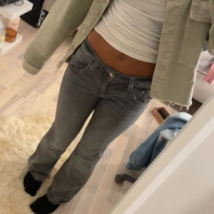 Grå bootcut jeans  - Säljer ett par grå jeans med bootcut-modell och snygga vita kontrastsömmar. Jeansen har låg midja, klassiska fickor fram och bak med knappdetalj på bakfickorna. Perfekta för dig som gillar en avslappnad men trendig look. Från Gina tricot storlek 164