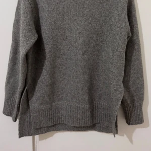 Grå stickad polotröja  - Säljer en grå stickad polotröja i storlek XS. Tröjan har ribbade detaljer vid krage, ärmslut och nederkant samt en hög polokrage med liten slits framtill. Perfekt för kyliga dagar och enkel att matcha med jeans eller kjol.