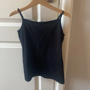 Svart linnetopp från H&M - En enkel svart linnetopp från H&M Basic, tillverkad i mjuk ekologisk bomull. Toppen har smala axelband och en rak, klassisk passform som funkar till allt. Perfekt att styla med jeans eller shorts för en chill look.