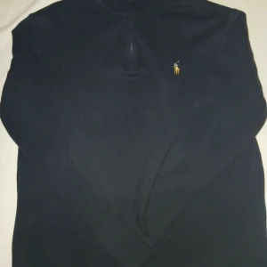 Svart half zip tröja Polo Ralph Lauren - Snygg marinblå långärmad tröja från Polo Ralph Lauren med half zip och klassisk broderad logga på bröstet. Tröjan har ribbade muddar och slits i sidorna för extra komfort. Perfekt för dig som gillar stilren och tidlös design.