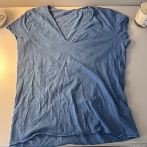 Blå v-ringad t-shirt från Zadig&Voltaire  - Blå t-shirt med v-ringning från Zadig&Voltaire . På ryggen finns ett meshparti med broderade stjärnor i samma blå ton. T-shirten har korta ärmar och är gjord i mjuk bomull,  Snygg detalj med broderad logga på sidan.