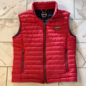 Röd dunväst från Colmar - Snygg klassik Colmar väst med quiltad design och hög krage. Plagget är i använt skick men har inte synliga defekter under användning. Nacken är lite missfärgad, inget stort ‼️. Annars är plagget i mycket bra skick och ”puffet” är fortfarande som ny🙌 Frågor? Hör av dig!