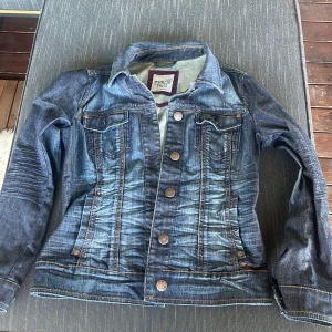 Blå jeansjacka från Esprit - Snygg blå jeansjacka från Esprit med klassisk passform, bruna kontrastsömmar och metallknappar framtill. Jackan har två bröstfickor med lock, sidfickor och coola slitningar för en avslappnad look. Perfekt till vår och sommar! Strl L på den men passar super på s/m 