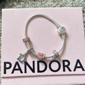 Pandora armband med berlocker - Snyggt silverfärgat armband från Pandora med flera berlocker, bland annat en sköldpadda med pärlemorskimrande kropp och en rosa blomma. Armbandet har även glittriga detaljer och runda berlocker med stenar. Perfekt för dig som gillar att mixa och matcha smycken.