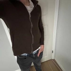 Brun kofta med dragkedja från Morris - Mörkbrun kofta från Morris med hel dragkedja framtill. Tröjan har lång ärm och är tillverkad i ett mjukt, stickat material. Tröjan sitter som en xs