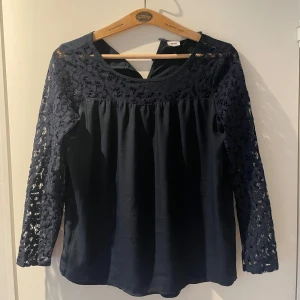 Mörkblå blus med spets från Object - Säljer en mörkblå blus från Object med vackra spetsdetaljer på ärmar och axlar. Blusen har rund halsringning. 