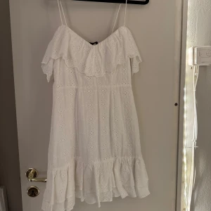 Studentklänning med broderade blommor - Superfin vit klänning med smala axelband, volang upptill och broderad spets över hela klänningen. Perfekt för srudenten!
