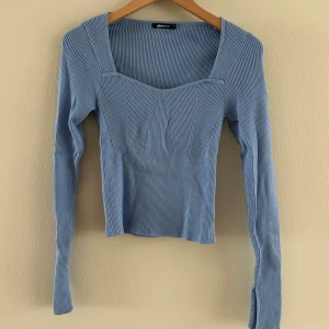 Ljusblå ribbad topp från Gina Tricot - Säljer en helt ny ljusblå ribbad topp från Gina Tricot med fyrkantig ringning och långa ärmar. Tröjan har en figurnära passform och slits vid ärmsluten för en extra detalj. Perfekt att styla med jeans eller kjol!