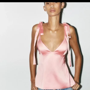 Rosa satinlinne med rosettband ZARA  - Säljer ett ljusrosa linnetopp i satin med smala axelband som knyts i rosetter. Toppen har djup v-ringning och figurnära passform, perfekt för sommaren. Den är från Zara med prislapp kvar 