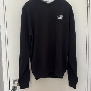 Svart tröja från Cutter & Buck - Svart långärmad tröja från Cutter & Buck med liten broderad logga på bröstet och ärmen. Klassisk passform och rund halsringning. Perfekt för en stilren och enkel look.