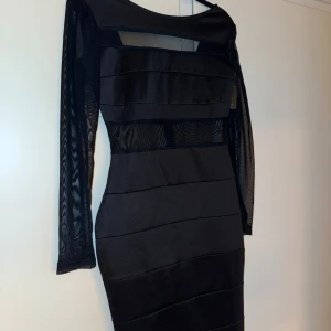 Svart långärmad klänning med meshdetaljer  - Säljer en svart långärmad klänning som slutar strax vid knäna. Klänningen har en kroppsnära passform och en snygg öppen rygg. 
