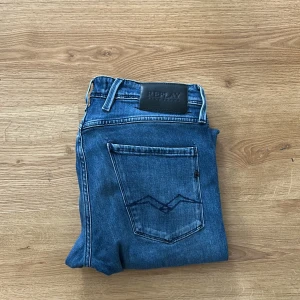 Blå Replay jeansbyxor - Säljer ett par klassiska blå jeans från Replay med raka ben och snygga detaljer på bakfickorna. Jeansen har normal passform och är tillverkade i ett slitstarkt denimtyg. Perfekta för dig som gillar stilrena och tidlösa jeans.
