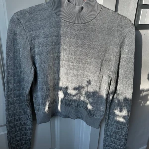 Grå stickad polotröja från Michael Kors - Säljer en snygg grå stickad polotröja från Michael Kors med diskret MK-mönster. Tröjan har hög krage och dragkedja bak i nacken. Perfekt för en stilren och trendig look. Helt ny aldrig använt säljer då den är för liten för mig! ❤️