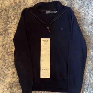 Mörkblå tröja med dragkedja från Polo Ralph Lauren - Säljer en mörkblå långärmad tröja från Polo Ralph Lauren med halv dragkedja och broderad logga på bröstet. Tröjan har en klassisk passform och är tillverkad i mjukt material, perfekt för kyligare dagar.