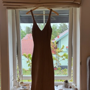 Beige ribbad långklänning med v-ringning - Säljer en beige långklänning med smala axelband och djup v-ringning. Klänningen är ribbad och har en figurnära passform som framhäver siluetten. Perfekt för varma dagar eller sommarens alla tillfällen.