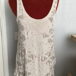 Beige linnetopp med mönster från Lindex M - Säljer en beige linnetopp från Lindex med geometriskt mönster och små glittriga detaljer. Toppen är ärmlös och har en djup urringning både fram och bak. Perfekt för varma dagar eller lager på lager. Mönstrat linne i viskos. Katter finns i hemmet!