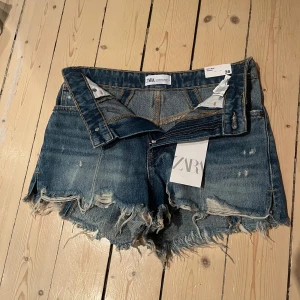 Blå jeansshorts från ZARA - Säljer ett par blå jeansshorts från ZARA med slitna detaljer. Perfekta för varma dagar och enkel att matcha med olika toppar. Helt nya med prislapp kvar, nypris är 29,95€ och går ej att få tag på i butik längre 