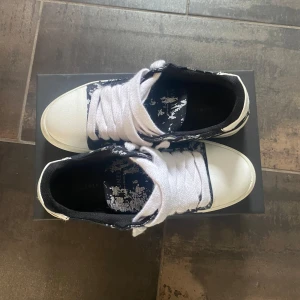 Numeris Pigment - Säljer ett par snygga sneakers från Numeris med svart och vitt mönster och vita snören. Skorna har en platt sula och rund tå, samt tydlig branding på hälen. Perfekta för dig som vill sticka ut med en unik look.