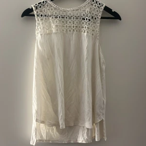 Vit ärmlös blus med spetsdetalj - Säljer en vit ärmlös blus med snygg spets upptill och rund halsringning. Blusen har ett luftigt fall och är perfekt för varma dagar. Passar lika bra till jeans som till kjol. Skriv för fler bilder!