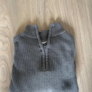 GRUNT, Grå stickad half zip, knappt använd  - Säljer en grå stickad tröja med halv dragkedja och hög krage. Tröjan har lång ärm och ribbade muddar vid ärmslut och nederkant. Perfekt för kyliga dagar och enkel att matcha med olika outfits.