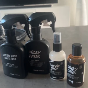 Fyra Lush-produkter: två body sprays, en leave-in och en duschgel - Säljer fyra olika Lush-produkter: Let The Good Times Roll body spray, Sticky Dates body spray, Super Milk leave-in conditioner och Sticky Dates duschgel. Alla flaskor har svart design med tydlig vit text och spray- eller pumpfunktion.