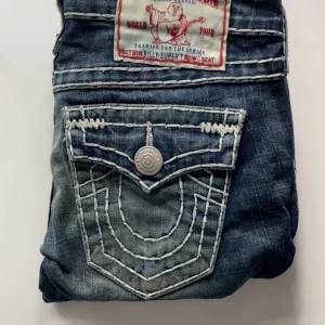 True Religion jeans med kontrastsömmar - Säljer jätte snygga true religion byxo som är i bootcut. Den har en lös tråd vid sidan men syns knappt. Säljer eftersom den är lite för lång på mig, Fråga om ni vill ha bilder på!