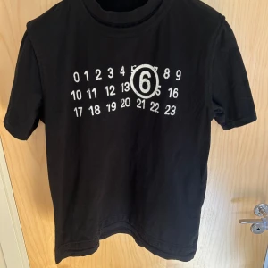Svart t-shirt från Maison Margiela - Cool svart t-shirt från Maison Margiela med deras ikoniska siffror. T-shirten har normal passform och är tillverkad i mjuk bomull. Perfekt för dig som gillar stilrena och unika plagg. Kvitto finns
