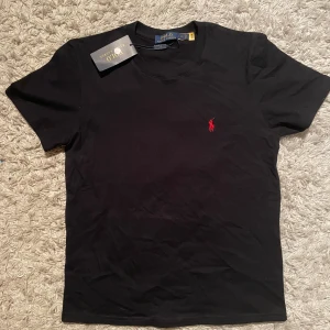 Polo Ralph Lauren T-shirt - Storlek M men sitter mer som S . Helt ny aldrig använd .Säljer en svart t-shirt från Polo Ralph Lauren med klassisk passform och rund hals. T-shirten har en liten röd broderad logga på bröstet och är tillverkad i mjuk bomull. Perfekt basplagg för garderoben.