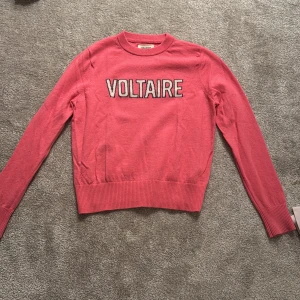 Rosa stickad tröja från Zadig & Voltaire - Säljer en rosa stickad tröja från Zadig & Voltaire med texten VOLTAIRE broderad framtill. Tröjan har rund halsringning och långa ärmar. Perfekt för dig som vill ha en snygg statementtröja!