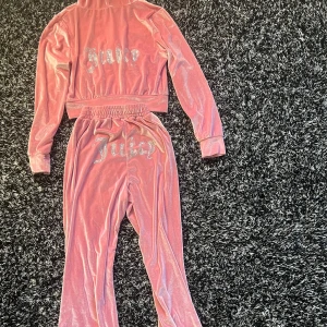 Rosa velourjacka med huva från Juicy Couture - Säljer ett rosa ej äkta juicy sätt, fickor på sidorna och glittrig Juicy-text på ryggen. Perfekt för en avslappnad och trendig look.