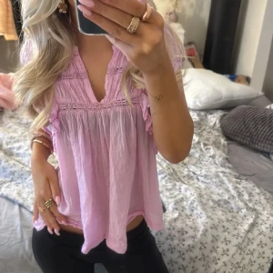 Ljusrosa blus med volangdetaljer - Söt ljusrosa blus med v-ringning och volangdetaljer längs ärmar och axlar. Blusen har korta ärmar och ett luftigt, löst sittande passform. Perfekt för vår och sommar. Lånade bilder💕