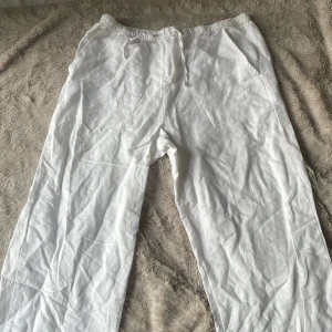 Vita linnebyxor med dragsko från Kappahl - Säljer ett par vita linnebyxor från Kappahl med elastisk midja och dragsko. Byxorna har raka ben och sidfickor, perfekta för varma dagar.
