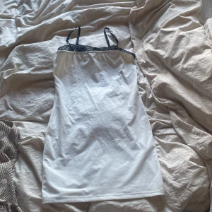 Vit kortklänning med svarta spetsdetaljer - Säljer en vit kortklänning med tunna axelband och svarta spetsdetaljer upptill.  och är perfekt för varma dagar. Kommer från shein och är aldrig använd då den var för stor för mig som har xs. 