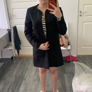 Svart kappa från H&M - Säljer en stilren svart kappa från H&M i storlek 38. Jackan har raka linjer, stora fickor framtill och är helsvart utan synliga knappar eller dragkedja. Perfekt för dig som gillar en minimalistisk look.
