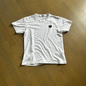Vit t-shirt från Comme des Garçons Play - Vit t-shirt med klassisk passform från Comme des Garçons Play, storlek M men passar S. Har det ikoniska svarta hjärta-logotypen broderad på bröstet. Perfekt basic med en stilren touch. Väldigt bra skick, säljer för den är för liten, kan tänka mig att byta mot en CDG tröja i strlk L
