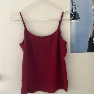 Röd linnetopp med smala axelband - Säljer en enkel och stilren röd linnetopp med smala axelband. Perfekt att matcha med jeans eller kjol för en snygg look. Tunt och mjukt material som känns skönt mot huden.