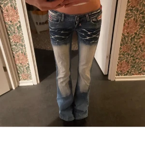 Blå bootcut jeans med slitningar och broderade detaljer - Säljer ett par blå bootcut jeans med ljusa slitningar och broderade detaljer framtill. Jeansen har låg midja och klassisk femficksdesign. Är lite nedtrampade längst ner (kom privat för bilder) men inget man tänker på! 
