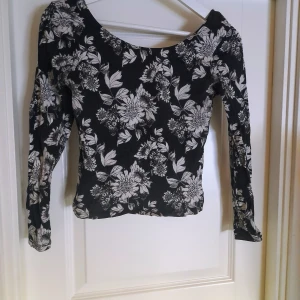 Svart blommig långärmad topp från Divided - Säljer en svart långärmad topp från Divided med vitt blommigt mönster. Toppen har en rundad halsringning och är figurnära i modellen. Perfekt för dig som gillar blommiga prints och vill ha en stilren men ändå iögonfallande topp. Djupare u-ringning i ryggen. Sparsamt använd. Men den har ytludd och är lite ljusare svart nyans än ny. Som det blir snabbt med mörka plagg