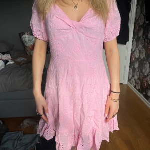 Rosa klänning med broderade detaljer - Söt rosa klänning med korta puffärmar, vringning, broderade blommönster och volang nertill. Perfekt för midsommar!! Lappen saknas men skulle säga det är en S🥰🥰